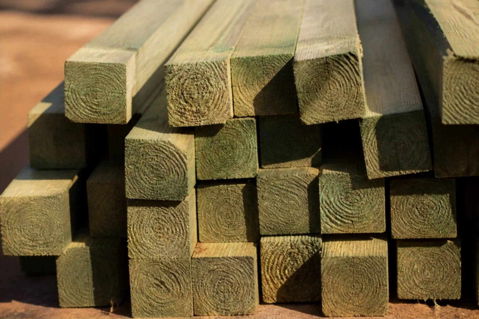 Stacked square treated fence posts showing the cut end grain